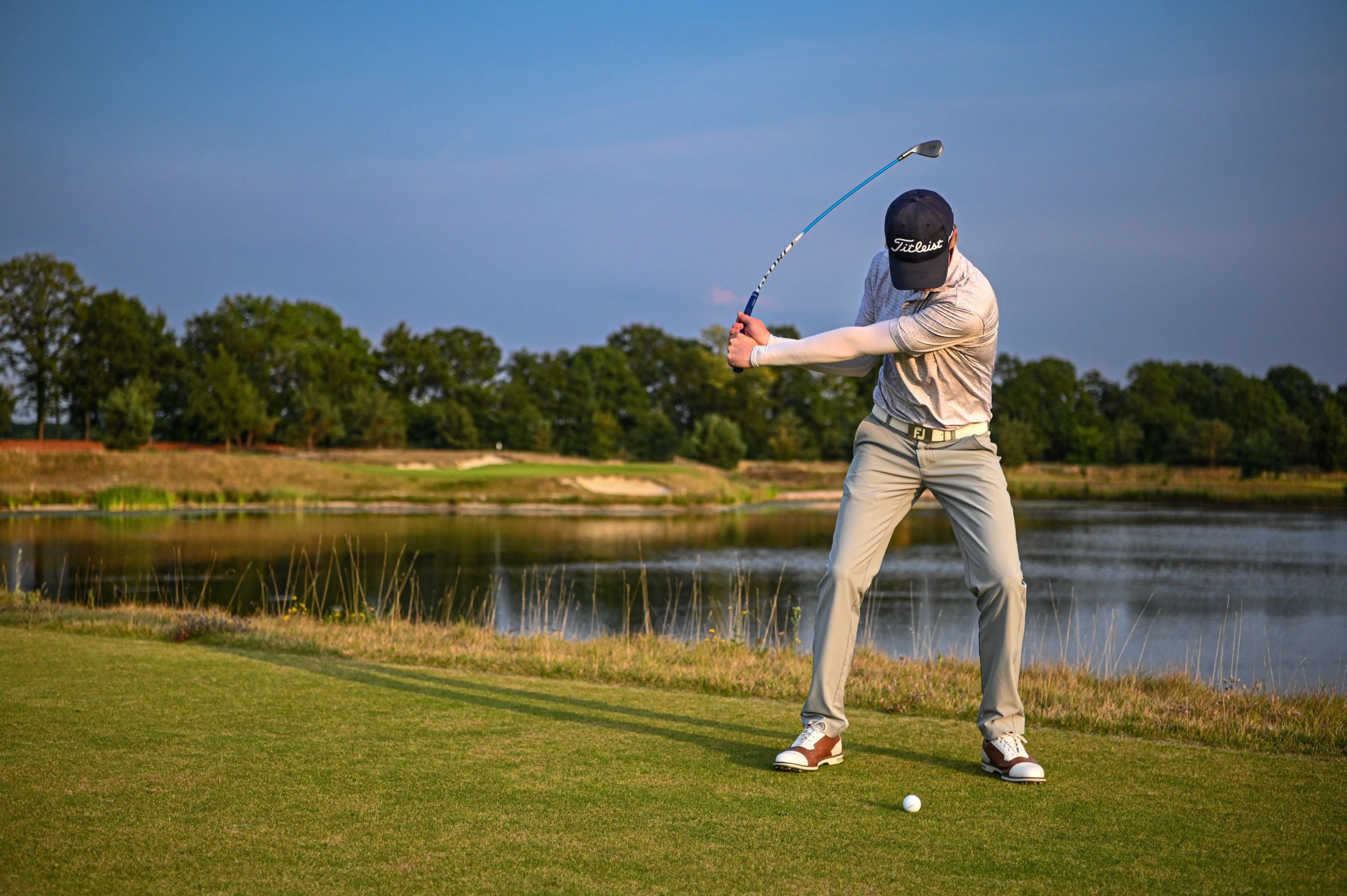 Pro golfer at a golf course swinging a gforce swing trainer 7 iron during the backswing